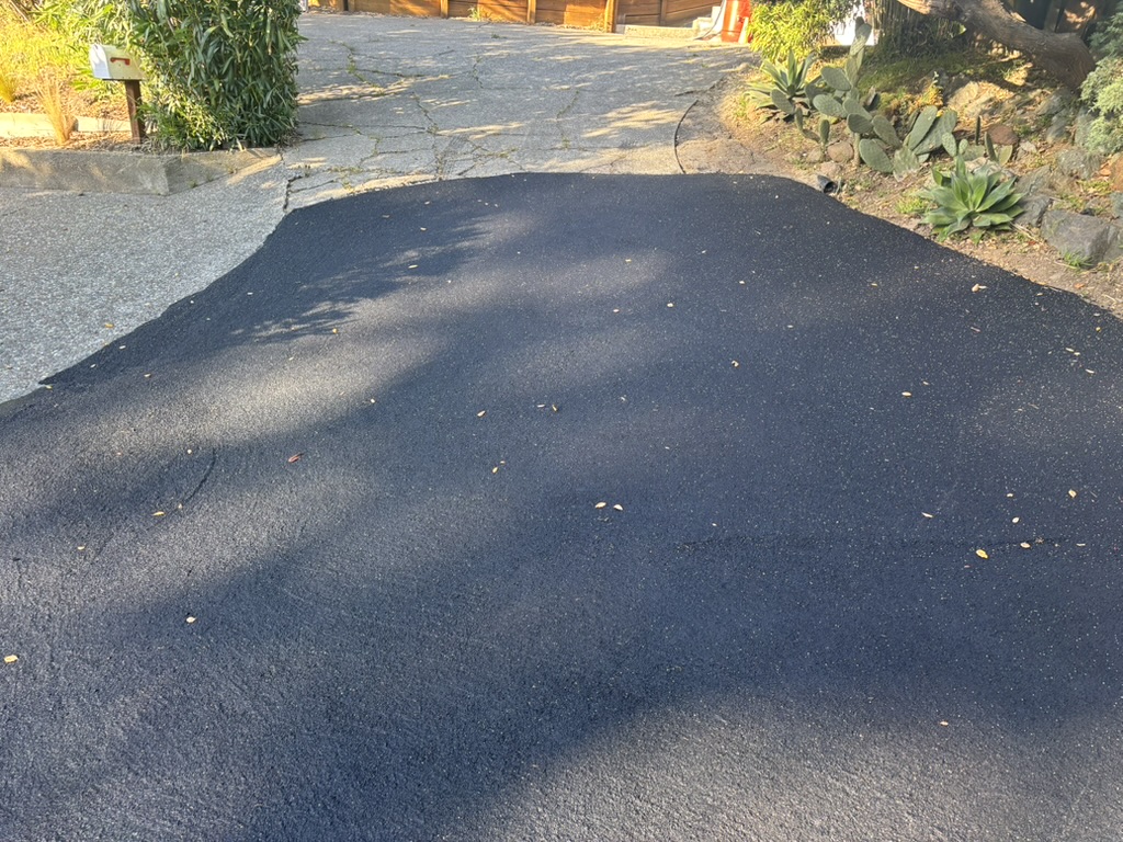 Slurry seal covering rough asphalt near a driveway entrance